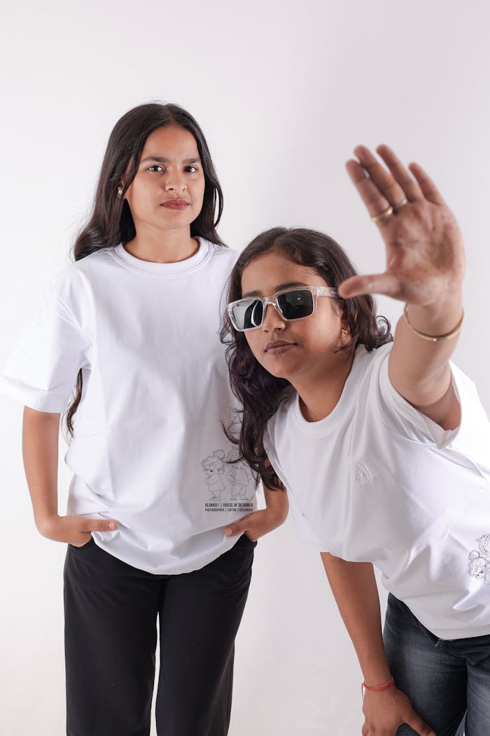 Stylish portrait of two young women in white t-shirts and sunglasses, posing in a studio in New Delhi, India.