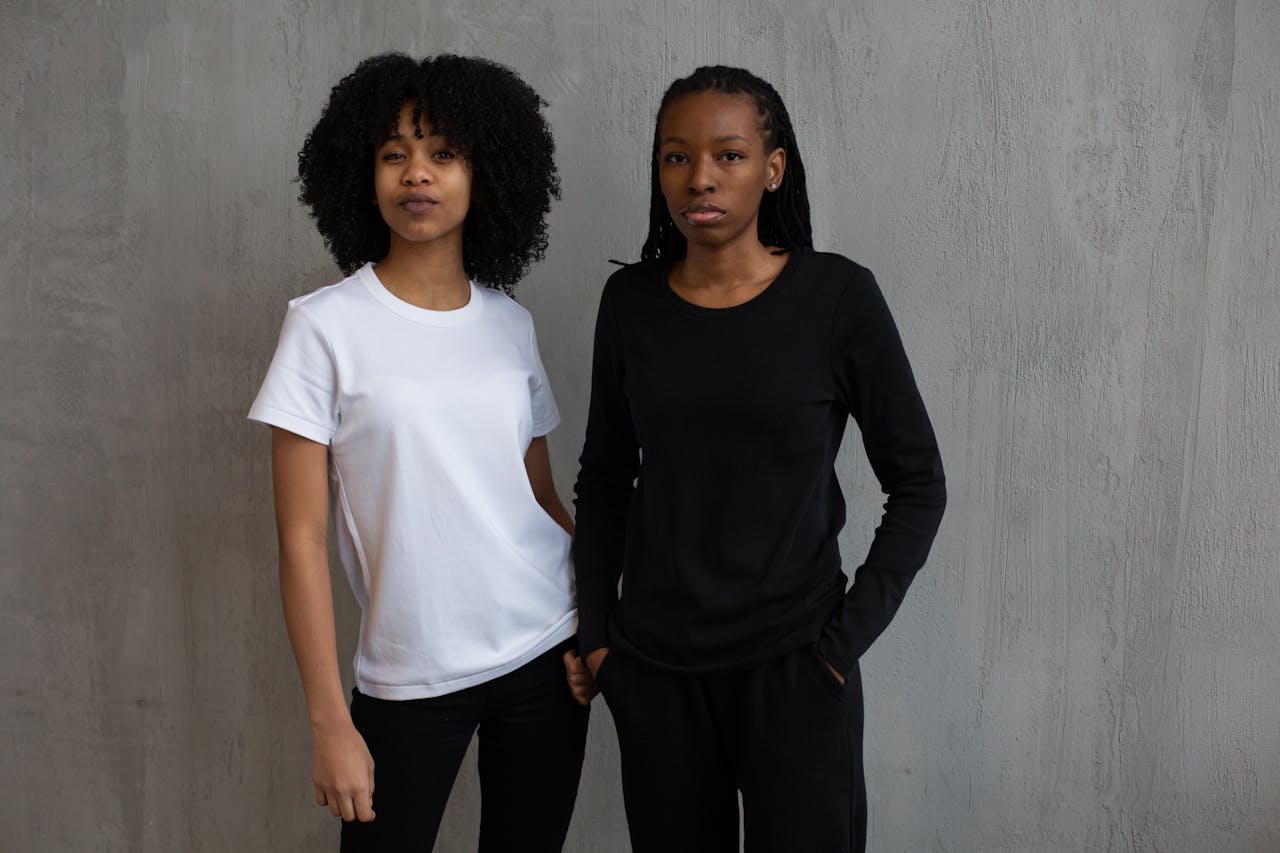 African American female model in black sports suit standing with hand in pocket near curly haired woman in t shirt