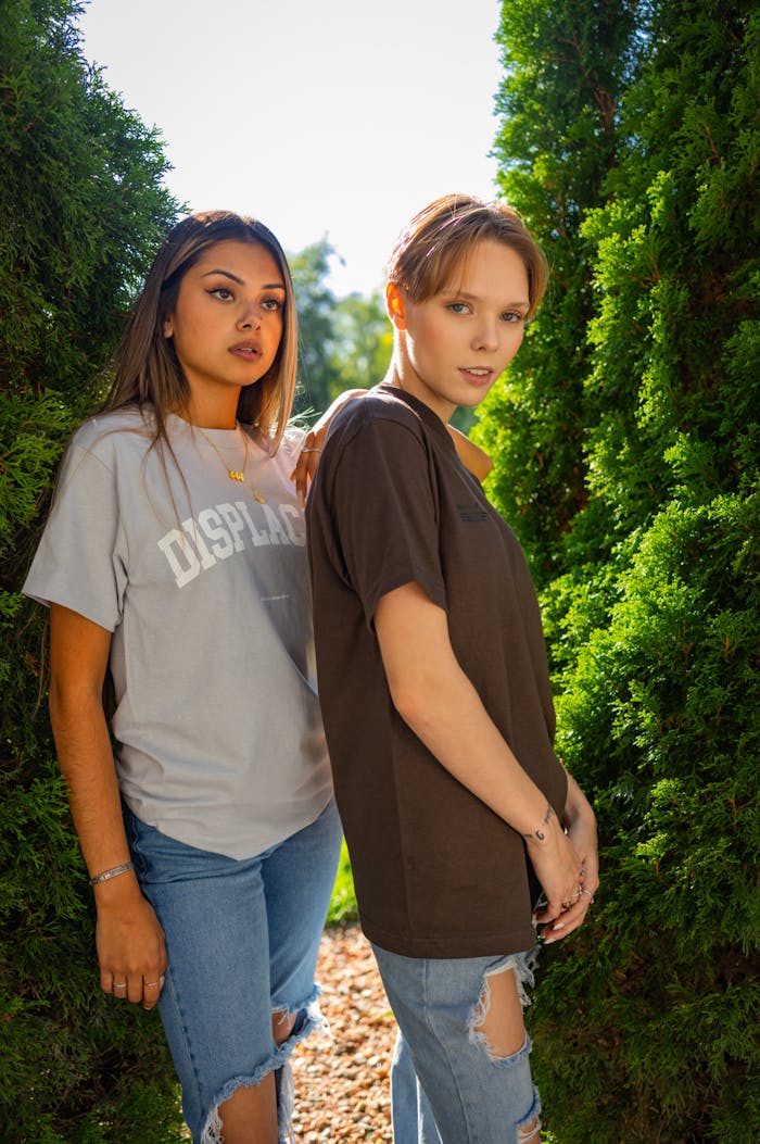 Two women in casual wear standing outdoors with greenery, showcasing friendship and style.
